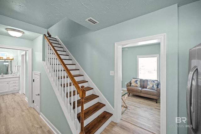 staircase with wood finished floors, visible vents, and baseboards