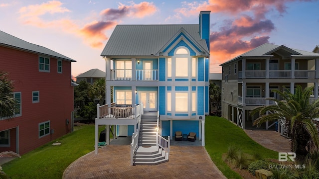 back of house at dusk with stairway, french doors, metal roof, a balcony, and a yard