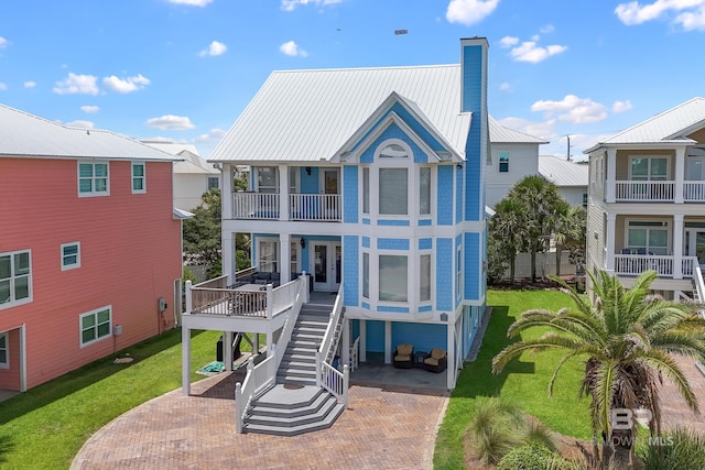 rear view of property featuring stairway, a lawn, a chimney, metal roof, and a balcony