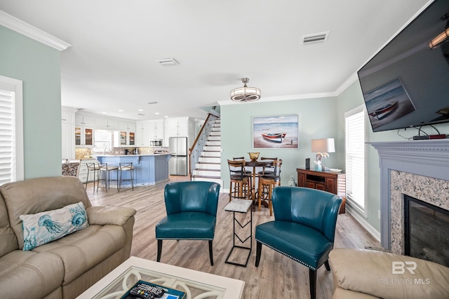 living area with visible vents, crown molding, stairs, light wood-style flooring, and a fireplace