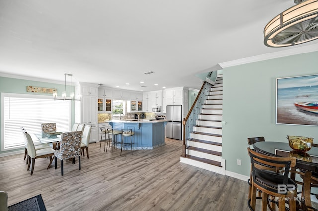 dining space featuring ornamental molding, light wood-style flooring, recessed lighting, stairway, and an inviting chandelier