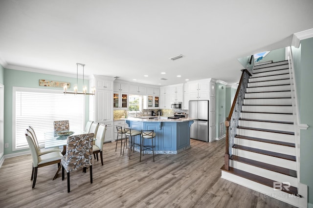 dining area featuring visible vents, ornamental molding, light wood finished floors, a chandelier, and stairs