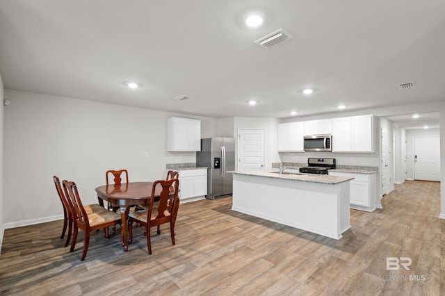 kitchen featuring sink, stainless steel appliances, white cabinets, light hardwood / wood-style flooring, and a center island with sink