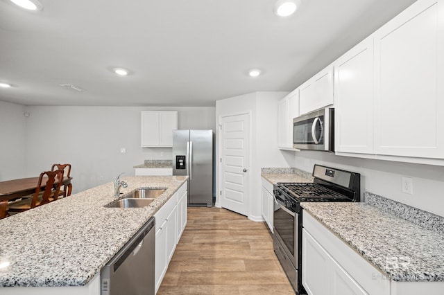 kitchen with an island with sink, white cabinetry, light wood-type flooring, sink, and stainless steel appliances