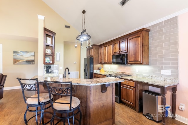 kitchen with light hardwood / wood-style floors, a kitchen bar, backsplash, light stone countertops, and black appliances