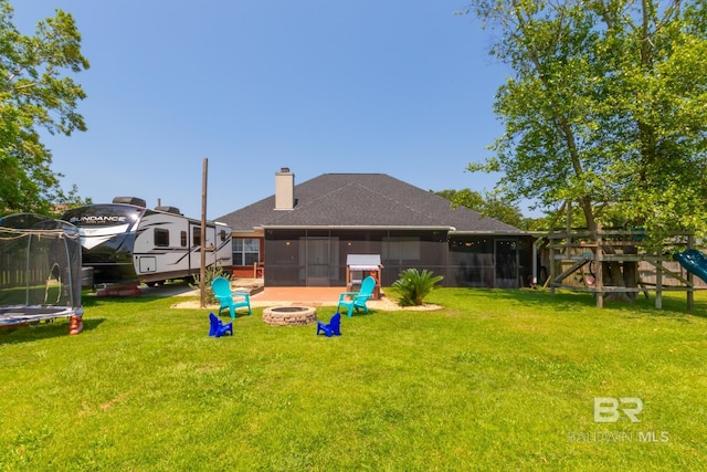 back of house featuring a trampoline, a playground, a sunroom, an outdoor fire pit, and a yard