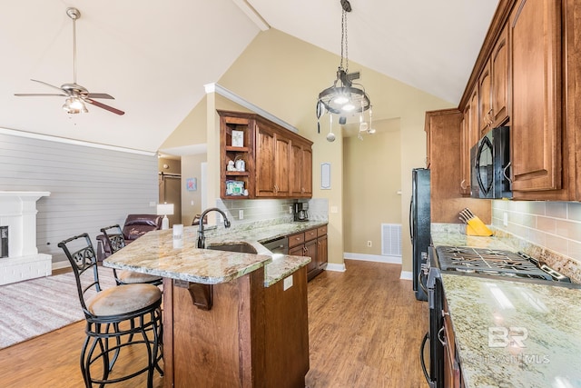 kitchen with tasteful backsplash, black appliances, a breakfast bar, sink, and light stone countertops