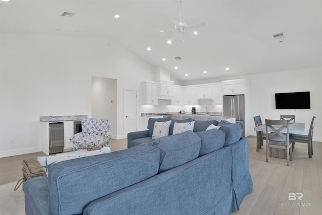 living room with light wood-style floors, beverage cooler, visible vents, and high vaulted ceiling