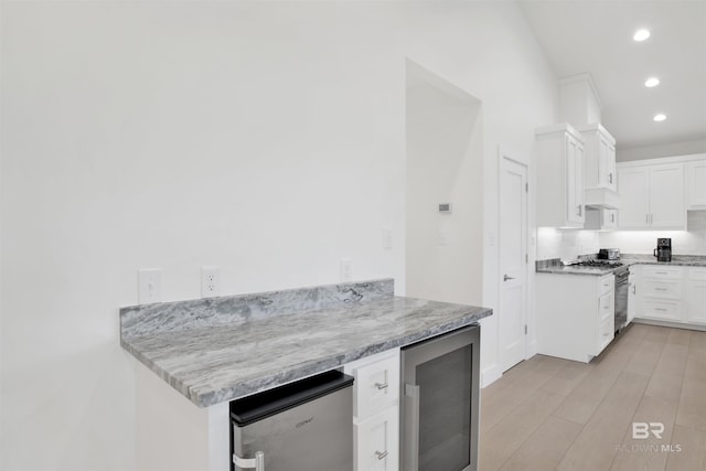 kitchen featuring wine cooler, tasteful backsplash, light wood-style floors, white cabinets, and gas range