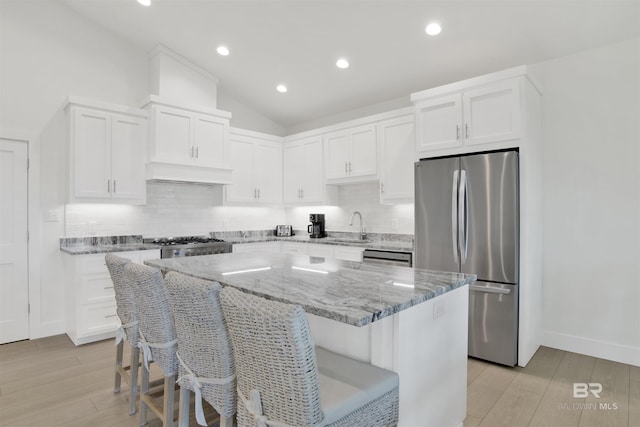 kitchen featuring light stone counters, freestanding refrigerator, white cabinets, a sink, and a kitchen island