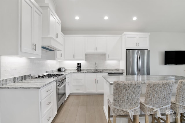 kitchen with a breakfast bar area, a sink, appliances with stainless steel finishes, light stone countertops, and custom range hood