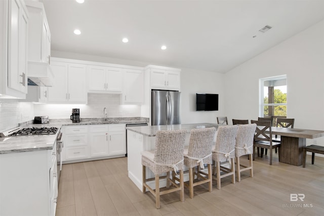 kitchen featuring stainless steel appliances, vaulted ceiling, custom exhaust hood, light stone countertops, and tasteful backsplash