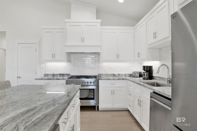 kitchen with tasteful backsplash, lofted ceiling, stainless steel appliances, white cabinetry, and a sink