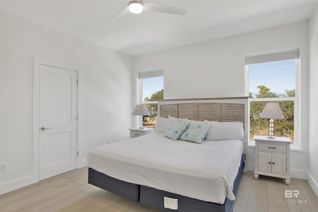 bedroom with a ceiling fan, multiple windows, light wood-style flooring, and baseboards