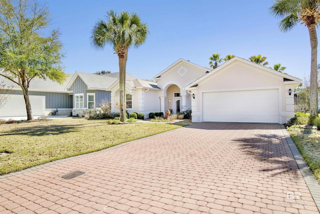 view of front of house with a front yard, decorative driveway, an attached garage, and stucco siding