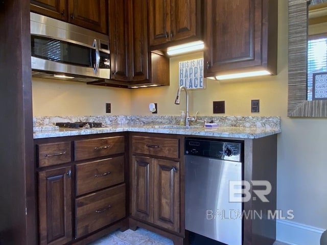 kitchen featuring dark brown cabinetry, appliances with stainless steel finishes, light stone countertops, and a sink