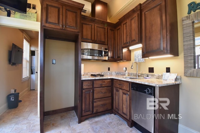 kitchen with stone finish floor, a sink, stainless steel appliances, baseboards, and light stone countertops