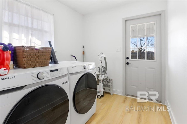 clothes washing area with washing machine and dryer, light wood-type flooring, and a healthy amount of sunlight