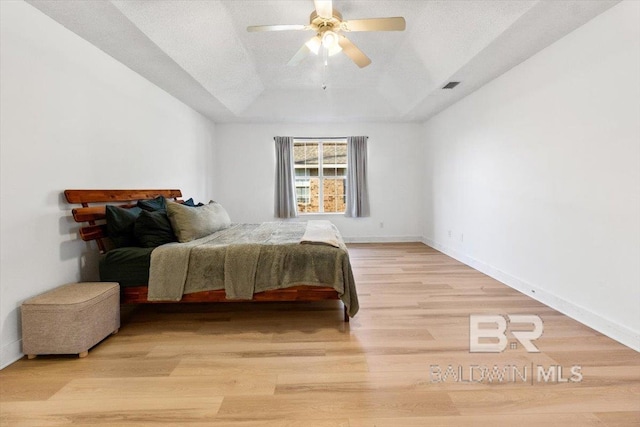 bedroom featuring a raised ceiling, light wood-type flooring, ceiling fan, and a textured ceiling