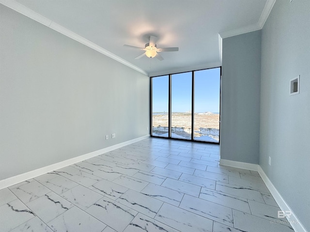 spare room featuring marble finish floor, ornamental molding, a ceiling fan, expansive windows, and baseboards