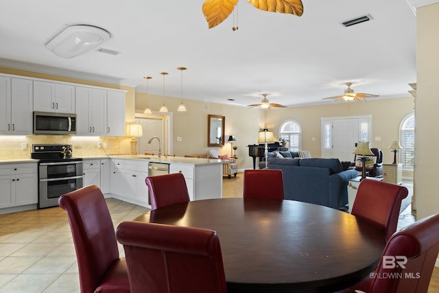 dining room featuring light tile patterned flooring, ceiling fan, crown molding, and sink