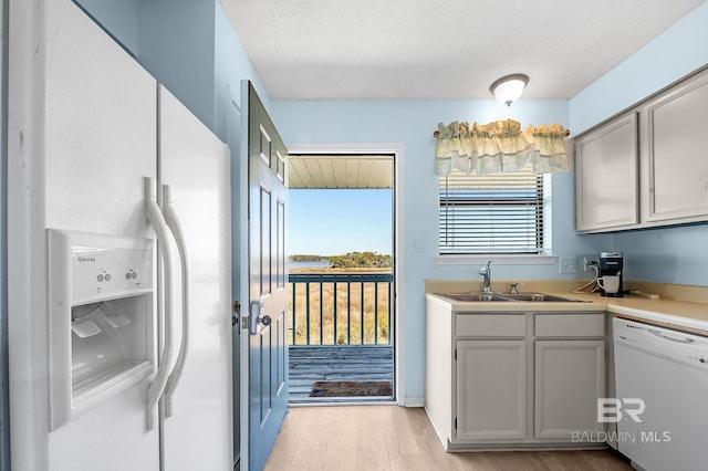 kitchen with white appliances, light wood finished floors, a sink, light countertops, and a textured ceiling