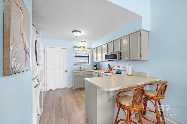 kitchen with stainless steel microwave, a breakfast bar, stacked washer and clothes dryer, a peninsula, and white electric range oven