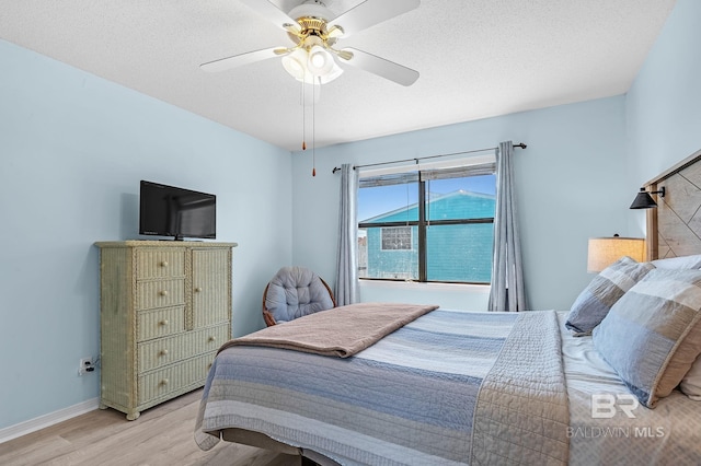 bedroom featuring ceiling fan, a textured ceiling, baseboards, and wood finished floors