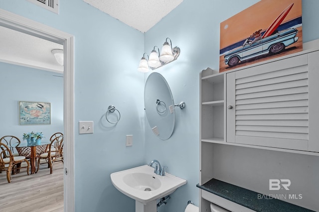 bathroom featuring visible vents, toilet, a sink, a textured ceiling, and wood finished floors