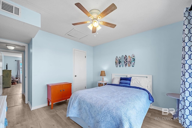 bedroom with visible vents, light wood finished floors, baseboards, attic access, and ceiling fan