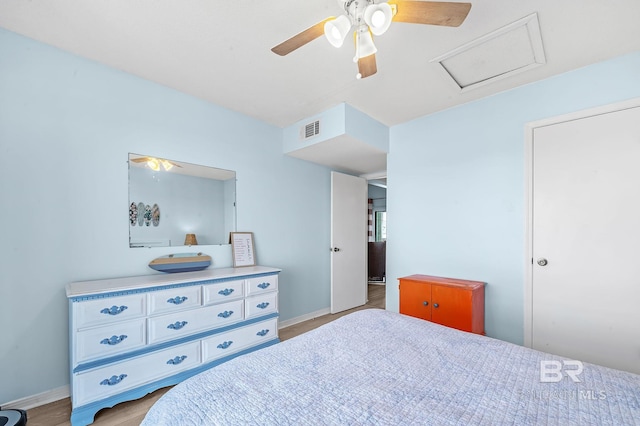 bedroom with visible vents, light wood-style floors, baseboards, attic access, and ceiling fan