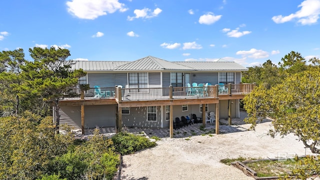 rear view of house featuring a wooden deck, metal roof, and a patio area