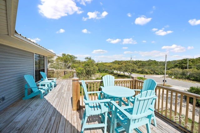 wooden terrace featuring outdoor dining area and view of wooded area