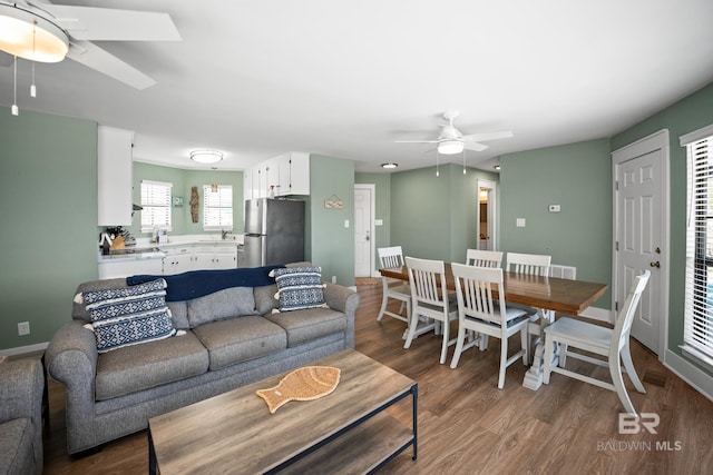 living area with a ceiling fan, wood finished floors, and baseboards