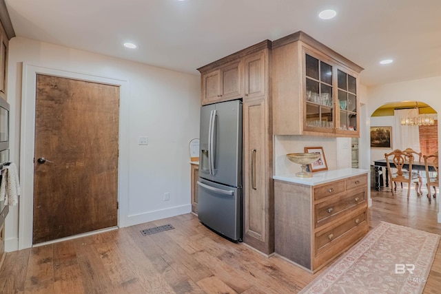 kitchen featuring an inviting chandelier, backsplash, stainless steel fridge, and light hardwood / wood-style floors