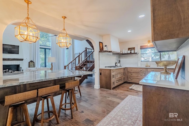 kitchen with gas stovetop, tasteful backsplash, custom range hood, pendant lighting, and light hardwood / wood-style floors