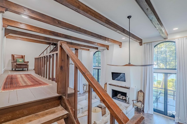 stairs with beamed ceiling, hardwood / wood-style floors, a brick fireplace, and a wealth of natural light