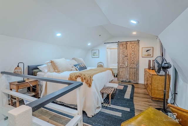 bedroom with lofted ceiling, a barn door, and light hardwood / wood-style flooring