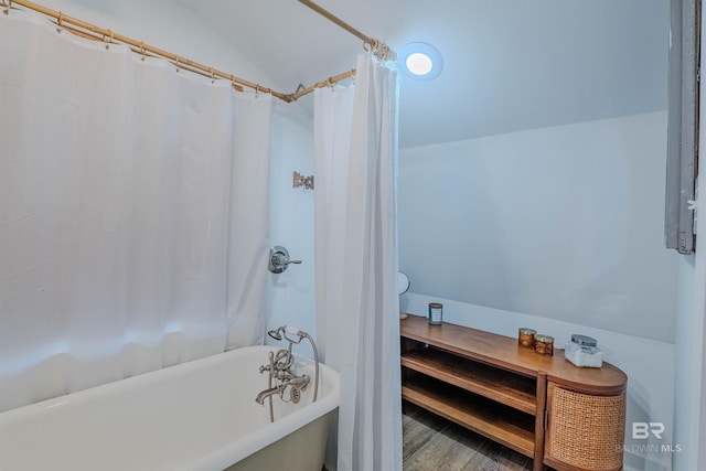 bathroom with a bath, vaulted ceiling, and wood-type flooring