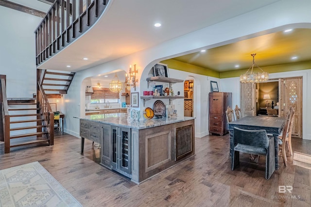 kitchen featuring a large island with sink, a notable chandelier, light stone counters, and decorative light fixtures