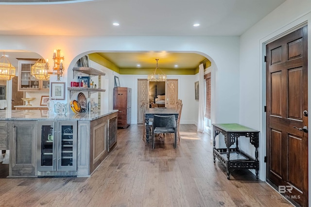 kitchen with an inviting chandelier, light stone counters, wood-type flooring, pendant lighting, and beverage cooler