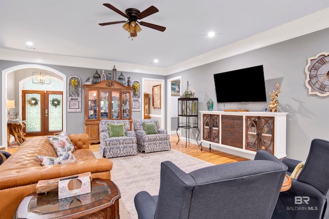 living room featuring ceiling fan with notable chandelier, light wood-type flooring, french doors, and crown molding