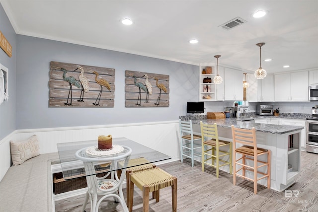 interior space featuring stone counters, light hardwood / wood-style flooring, decorative light fixtures, stainless steel appliances, and kitchen peninsula