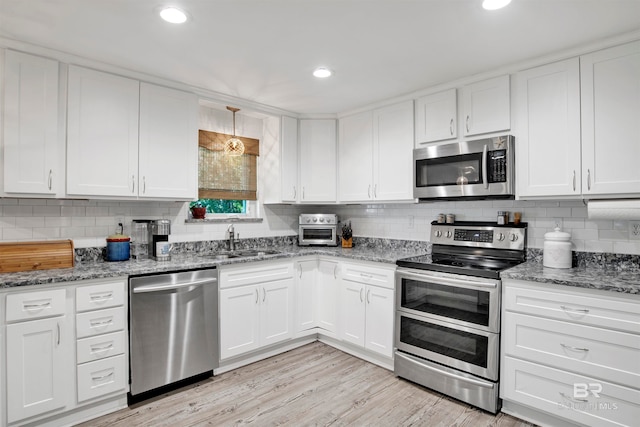 kitchen featuring appliances with stainless steel finishes, light stone counters, light hardwood / wood-style floors, and sink