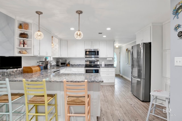 kitchen featuring light wood-type flooring, appliances with stainless steel finishes, kitchen peninsula, pendant lighting, and a breakfast bar