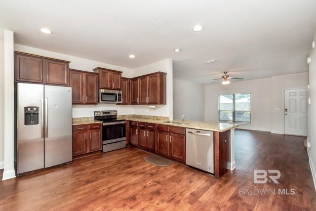 kitchen featuring ceiling fan, wood-type flooring, light stone countertops, kitchen peninsula, and stainless steel appliances