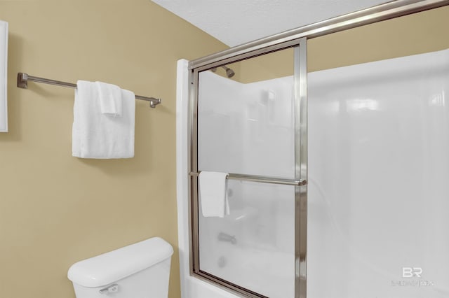 bathroom featuring bath / shower combo with glass door, toilet, and a textured ceiling