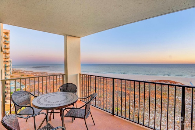 balcony at dusk with a water view and a view of the beach