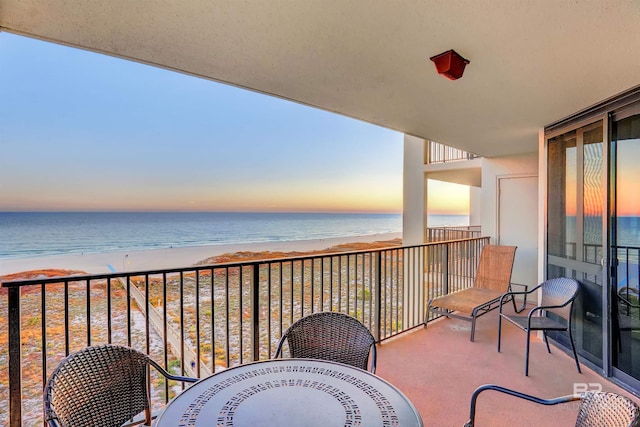 balcony at dusk featuring a beach view and a water view