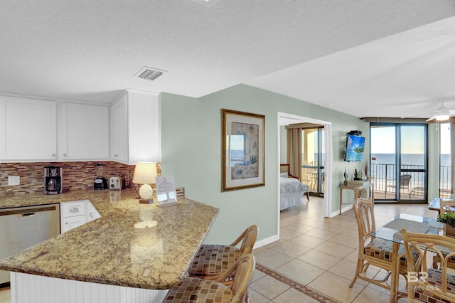 kitchen with stainless steel dishwasher, light tile patterned floors, kitchen peninsula, and light stone countertops